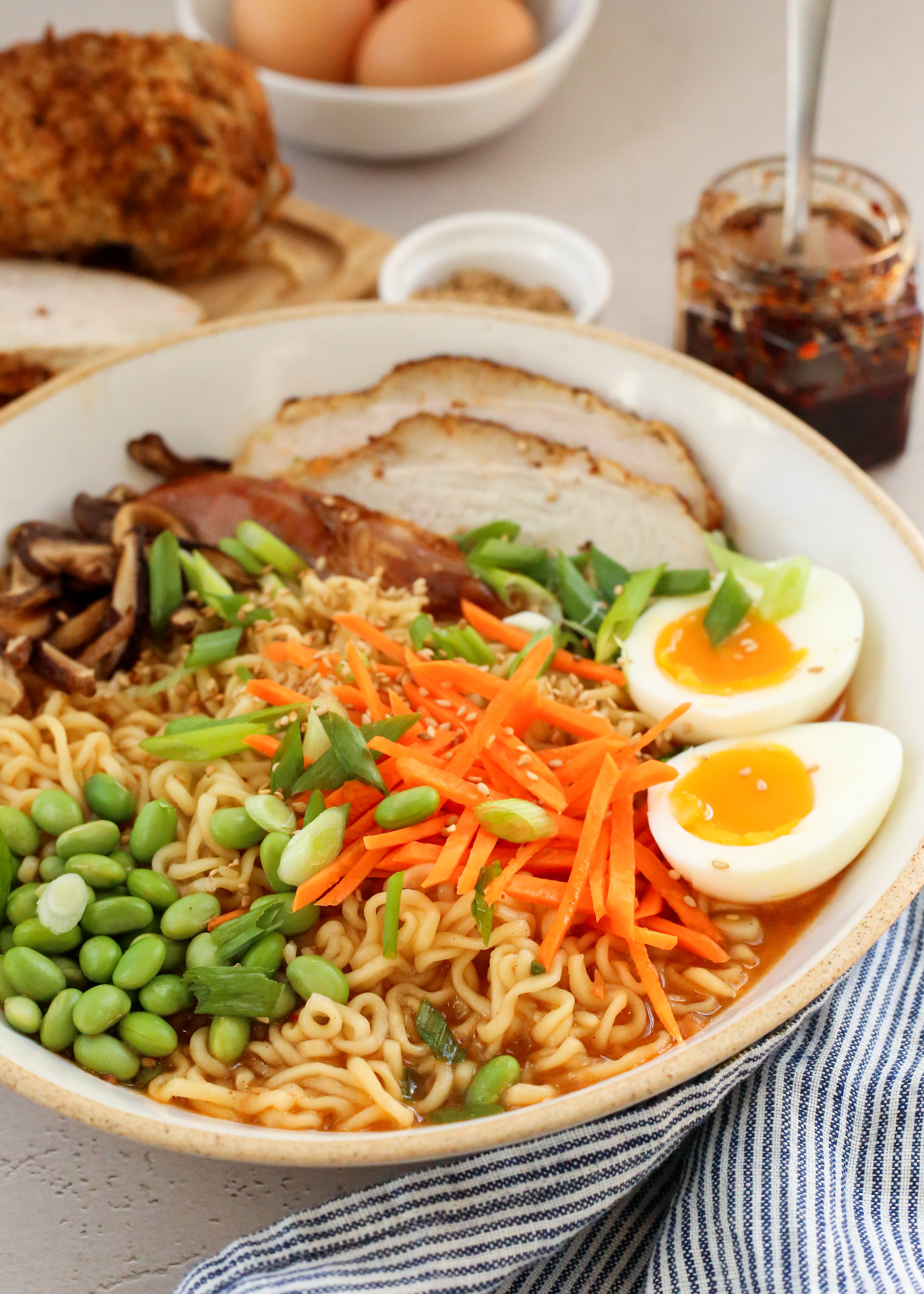A full bowl of leftover turkey ramen displayed in a kitchen scene, with the colorful veggies standing out against the noodles, broth, and sliced turkey with soft boiled 7 minute eggs sliced and placed inside the bowl on the right side