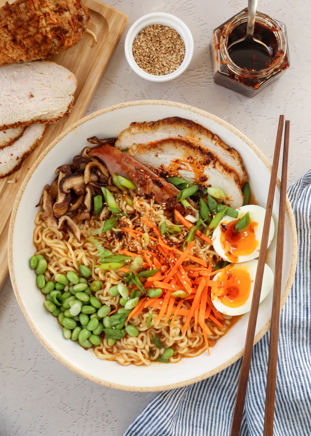 Overhead image of a bowl of leftover turkey ramen, with thick slices of roasted turkey resting inside a ramen bowl topped with carrots, edamame, soft boiled 7 minute eggs, green onions, and mushrooms and a drizzle of chili oil on top