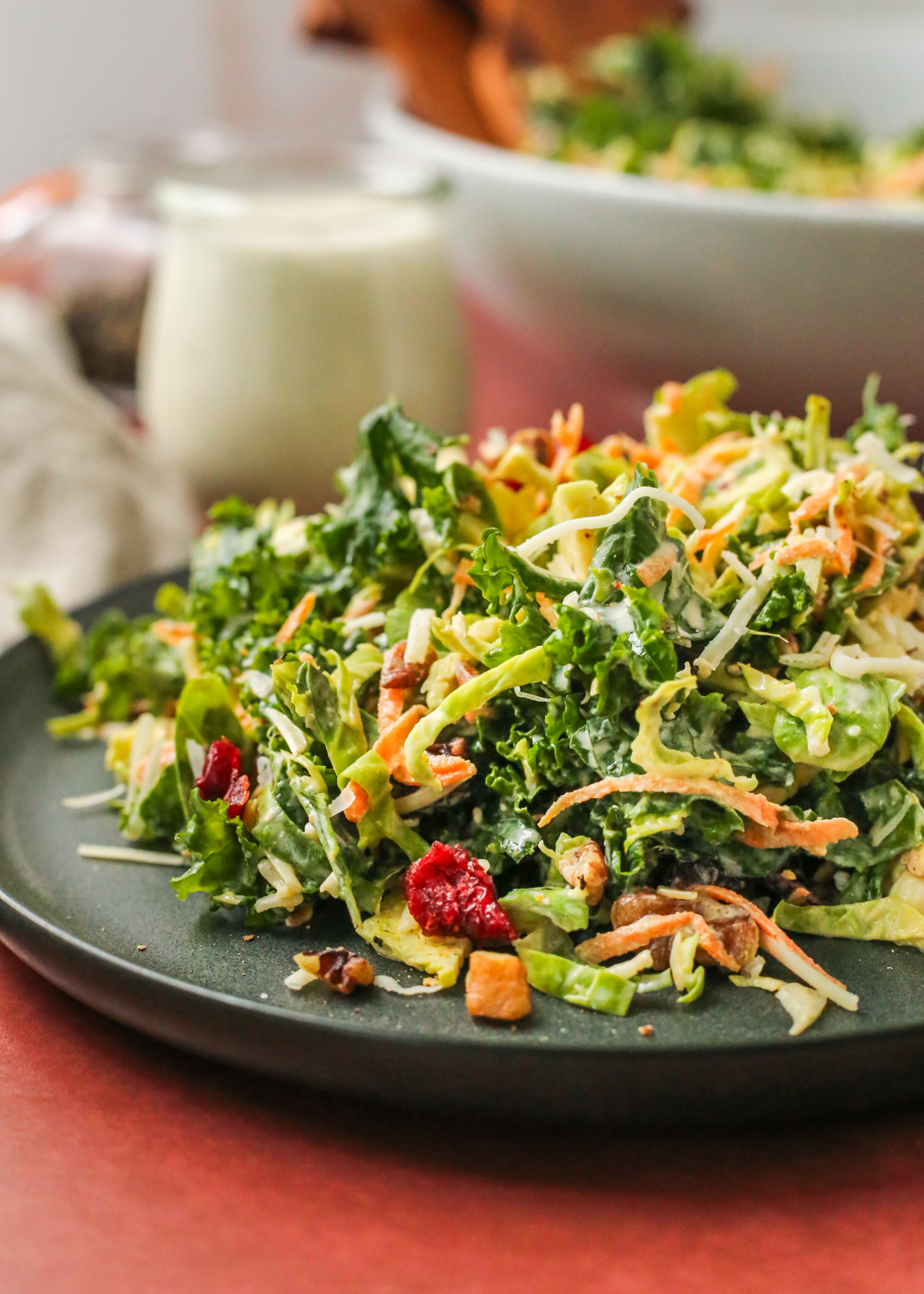 A close side view of a kale and brussels sprout salad, featuring shredded carrots, dried cranberries, and chopped nuts mixed throughout with everything tossed in a creamy white dressing