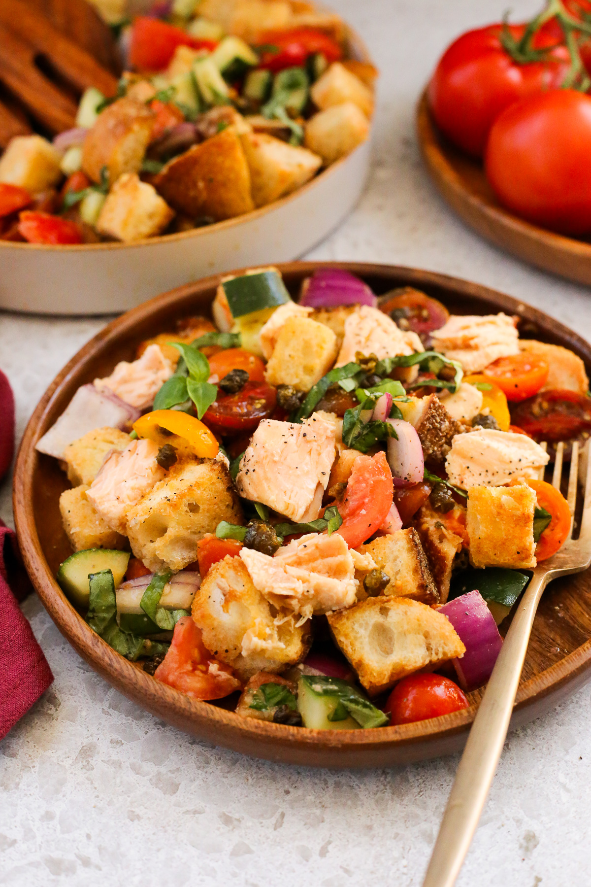 A beautiful and colorful panzanella salad is plated and served with a fork, with the remainder of the prepared salad in the background along with extra tomatoes. 