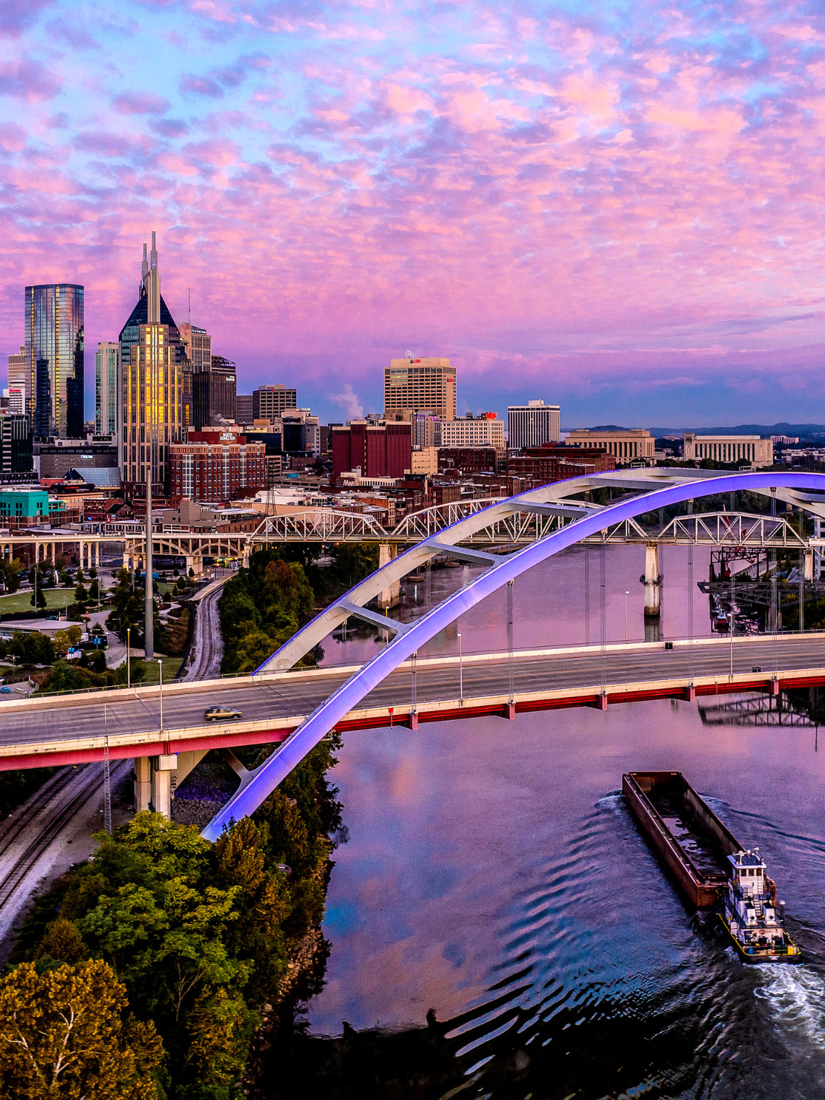 A sunset view of downtown Nashville, with recognizable landmarks such as the river and pedestrian bridge. 