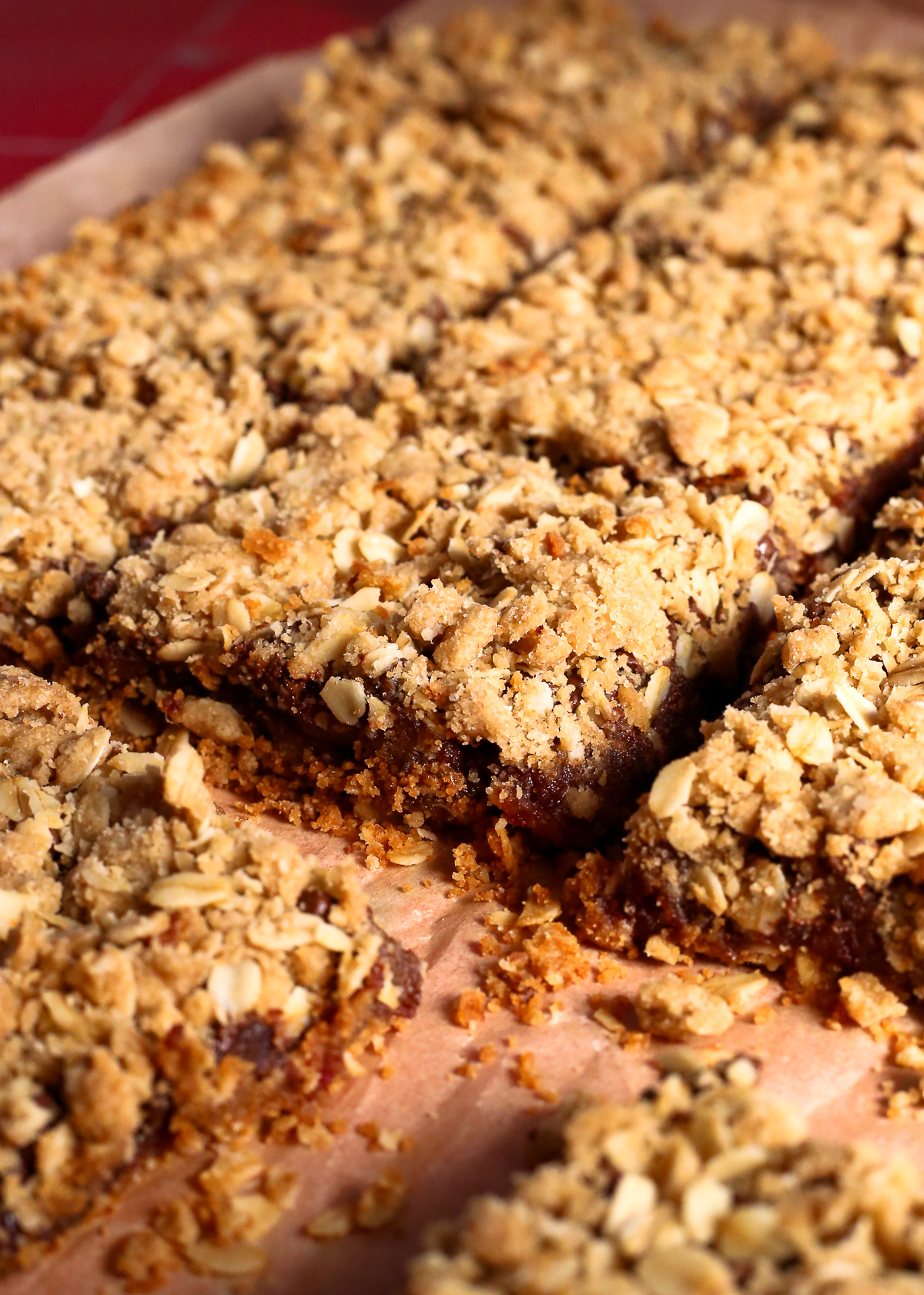A batch of old fashioned date bars, cut into squares and displayed on a piece of parchment paper to show the crumbly layers and sticky date filling. 