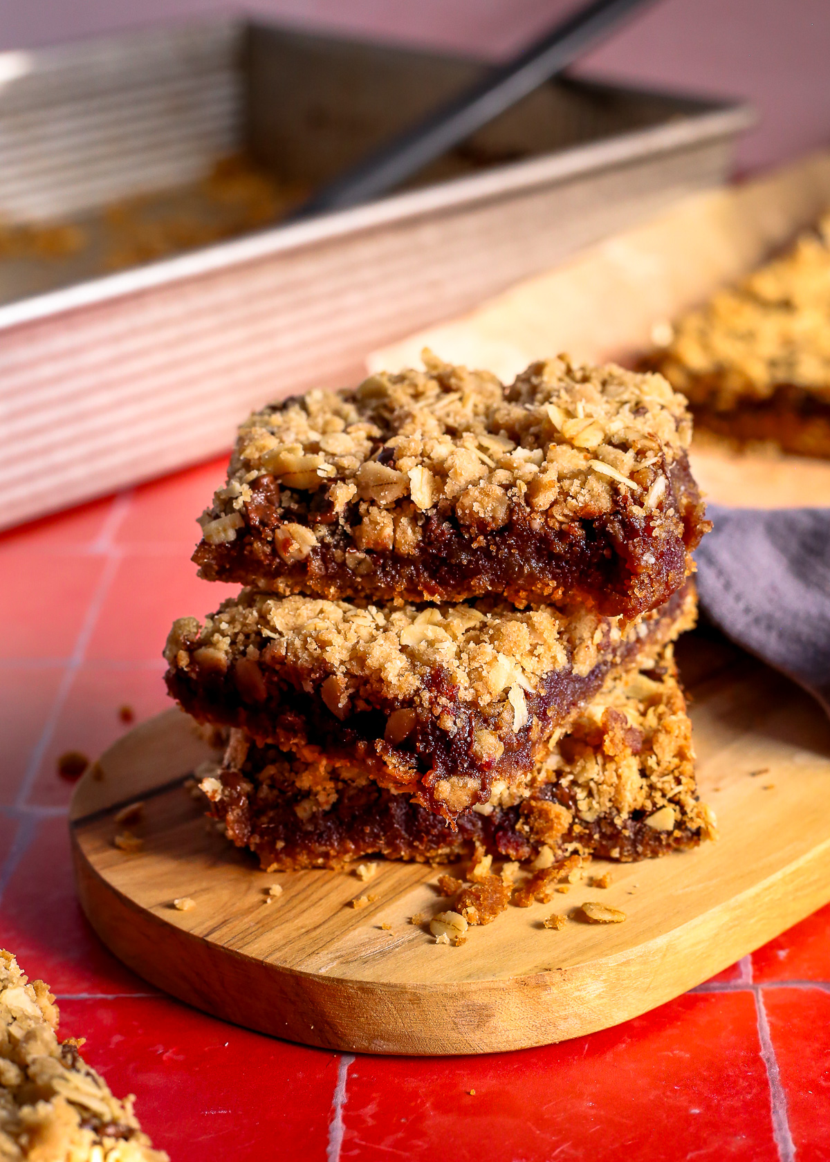 A stack of three old fashioned date bars on a bright red til countertop, looking crumby and sticky as if just freshly baked. 