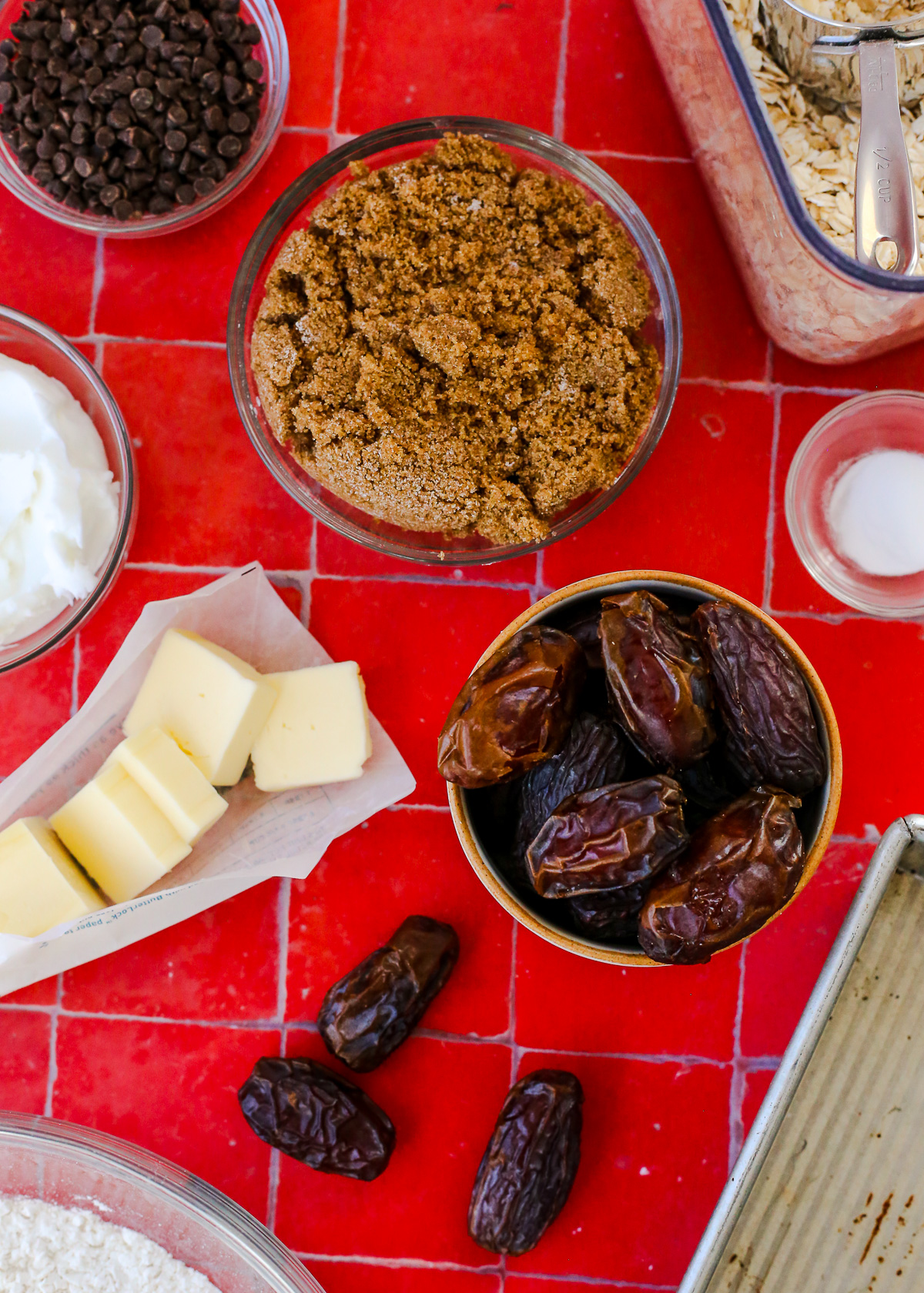Assortment of ingredients needed to make a date bar recipe, including fresh whole dates, brown sugar butter, flour, oats, mini chocolate chips, and shortening. 