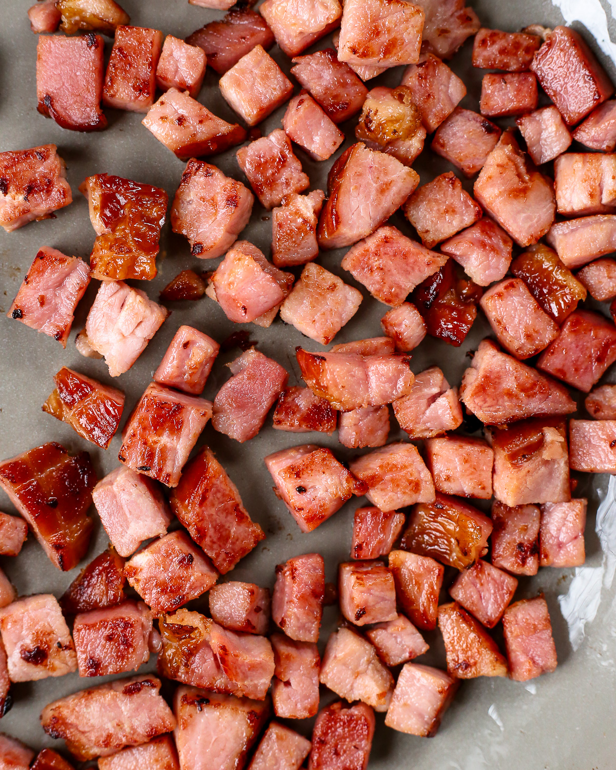 A close view of the seared ham, cut into similar sized small pieces, lightly seared in a large skillet with browned edges.