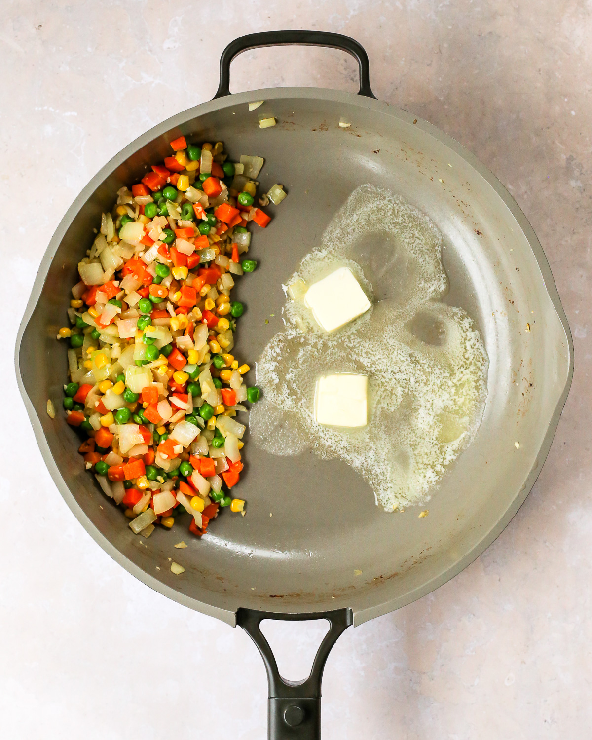 The cooked vegetable mixture is pushed to the left side of the skillet as two pats of butter melt on the open right side of the same skillet.