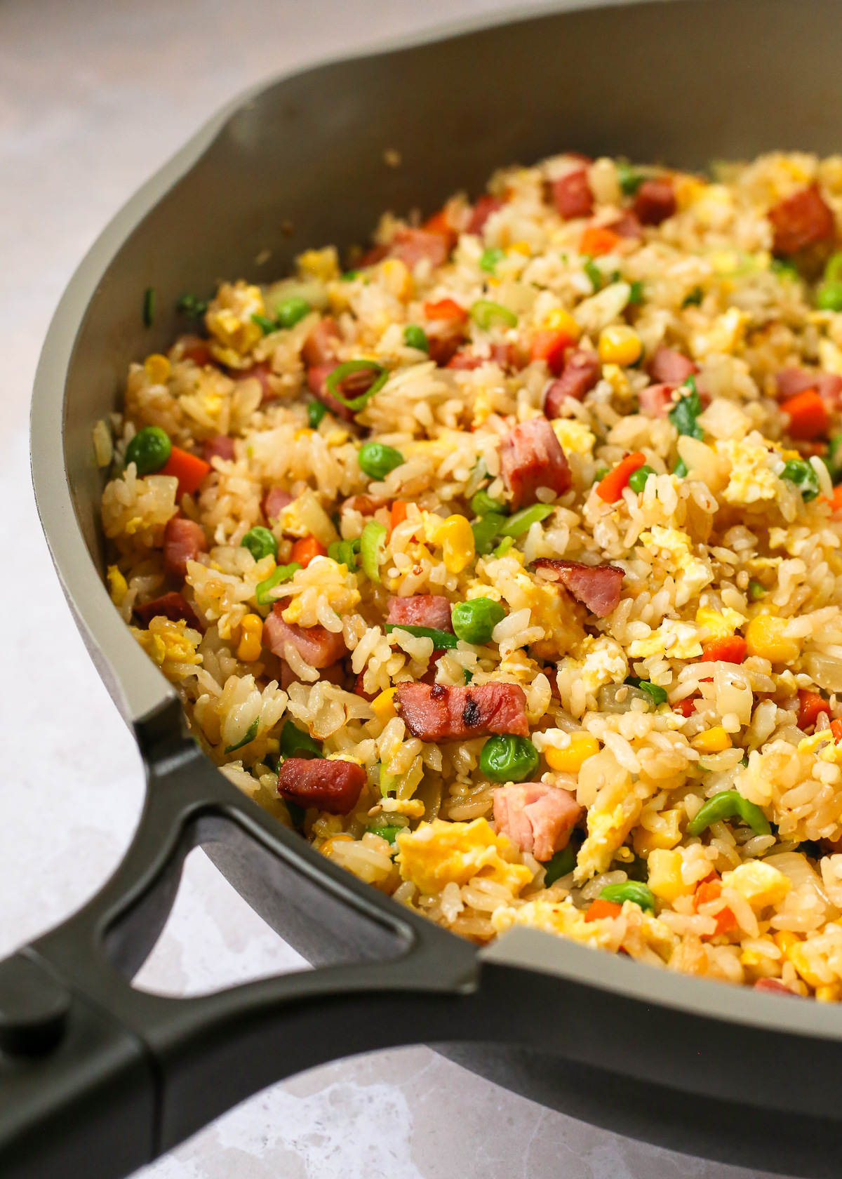 A view in to the large skillet used to make a ham fried rice recipe, with the rice lightly fried and colorful veggies, diced ham, and scrambled eggs mixed evenly throughout.