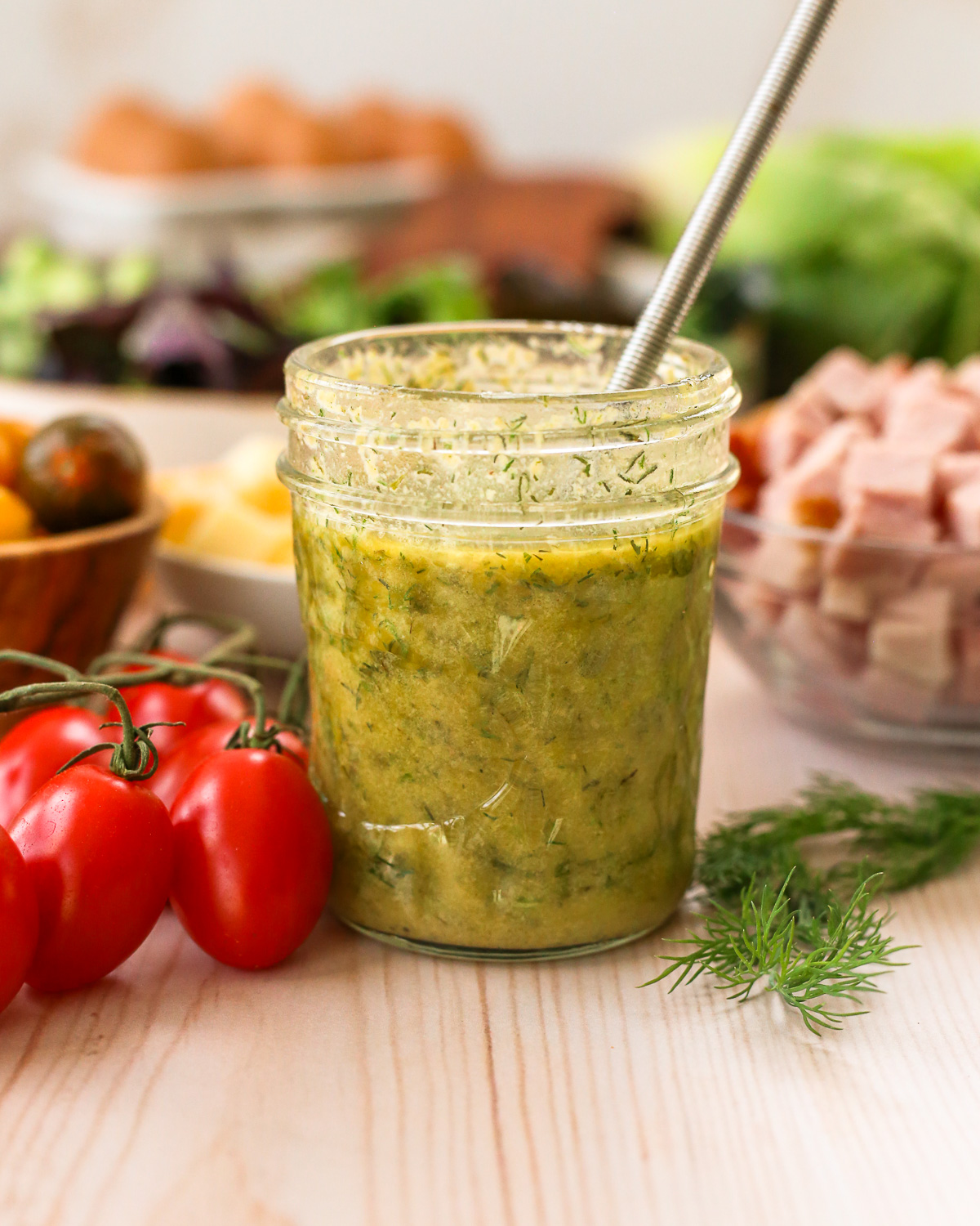 A freshly mixed ranch vinaigrette, surrounded by fresh vegetables and salad ingredients.