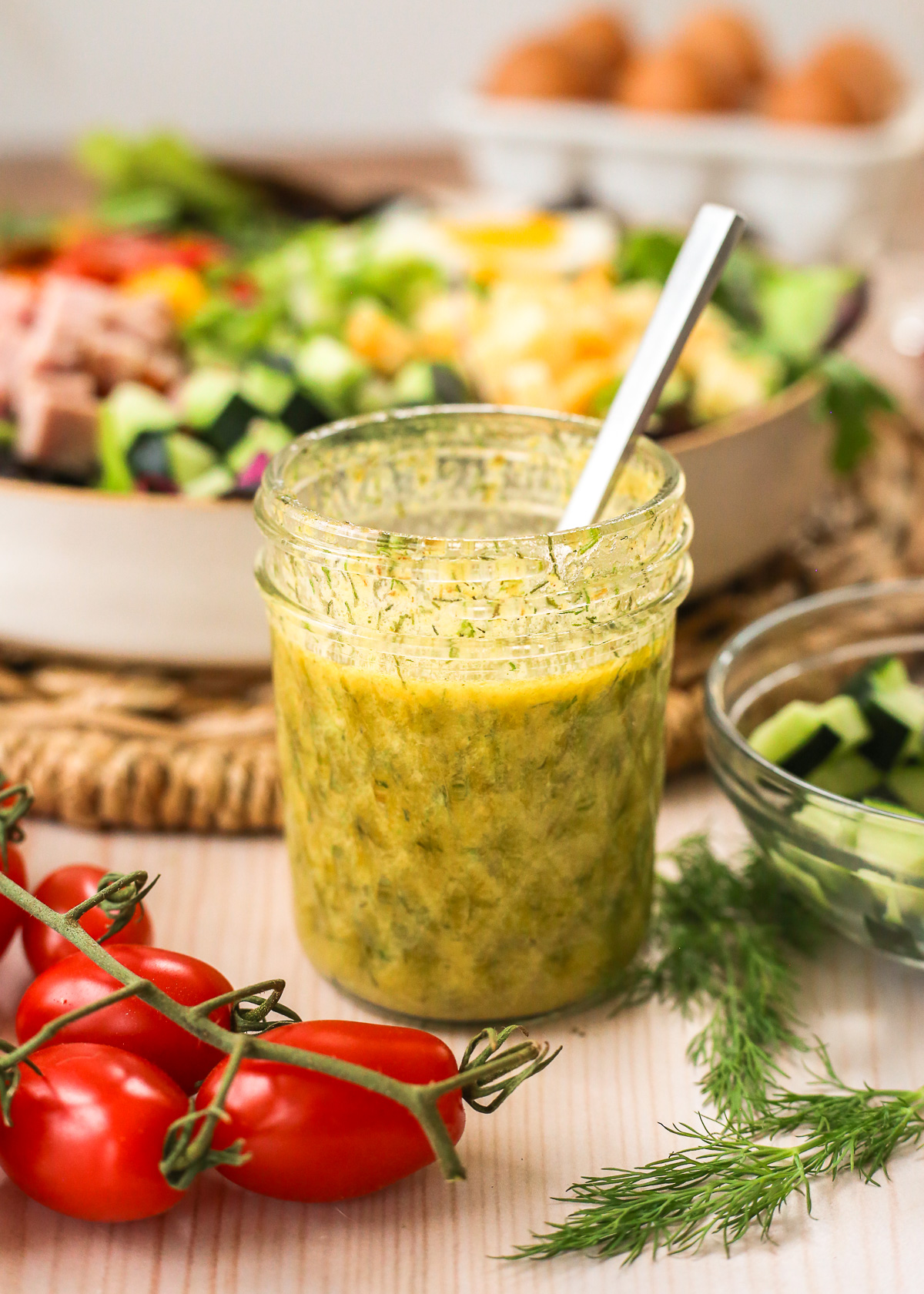 A small glass jar of homemade ranch vinaigrette displayed in front of a colorful salad on a kitchen table.