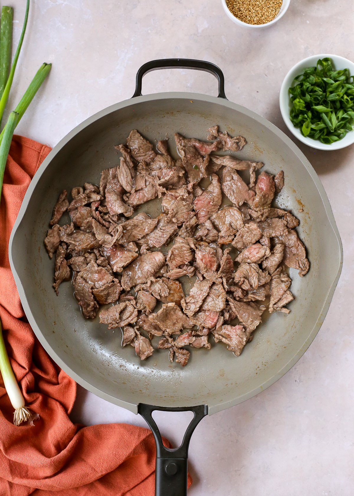 Overhead view of a large nonstick skillet used to stir fry thinly sliced beef, with some bits showing browned edges.