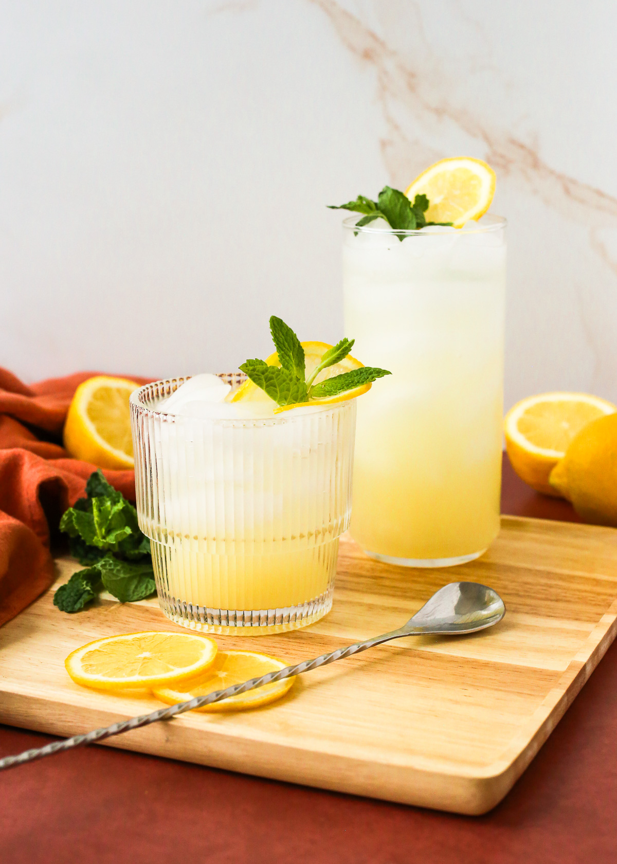 Two full glasses of yuzu lemonade displayed on a brightly lit kitchen countertop, both garnished with fresh mint and a slice of lemon.
