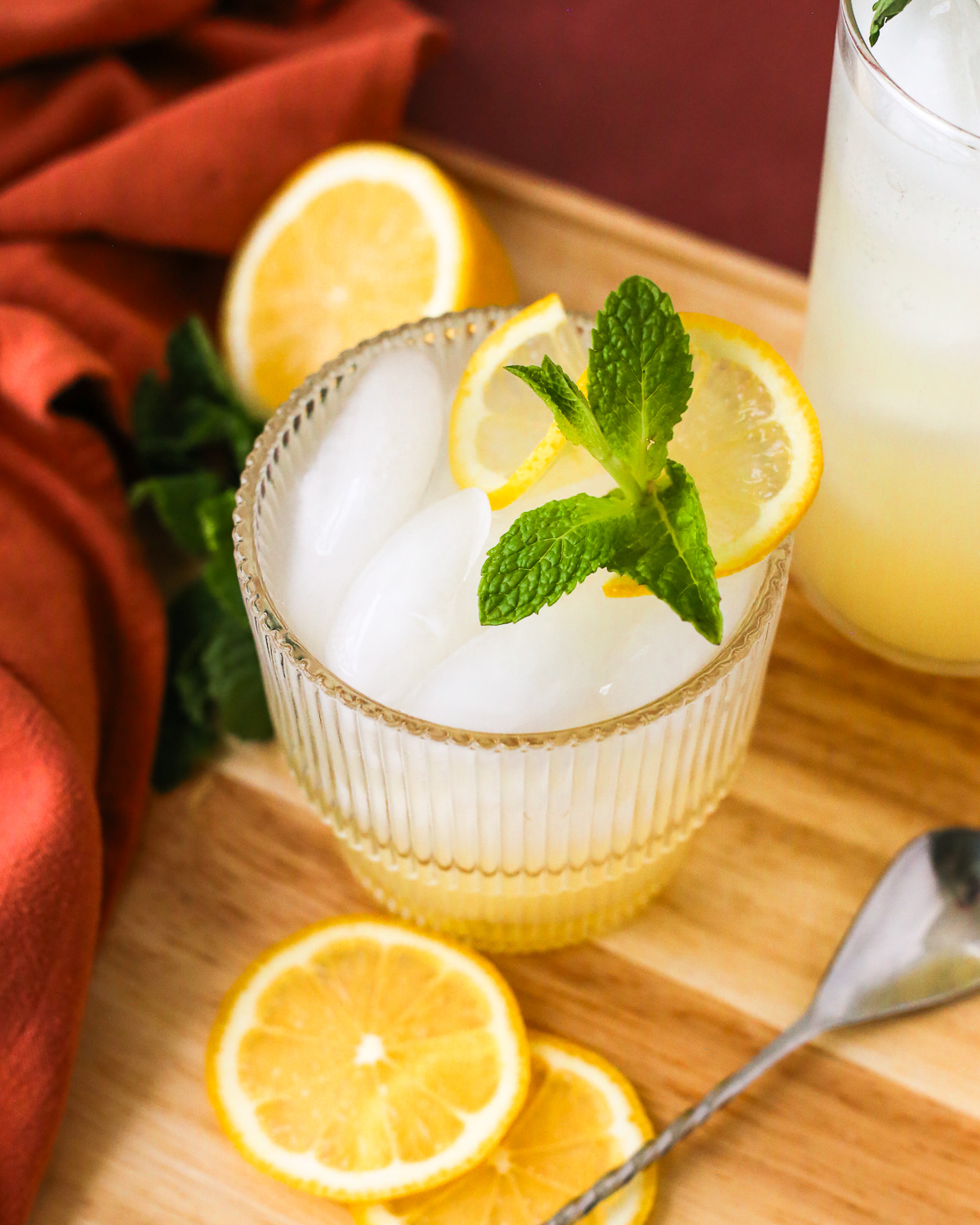 A large glass of yuzu lemonade garnished with a sprig of fresh mint, surrounded by slices of lemon.