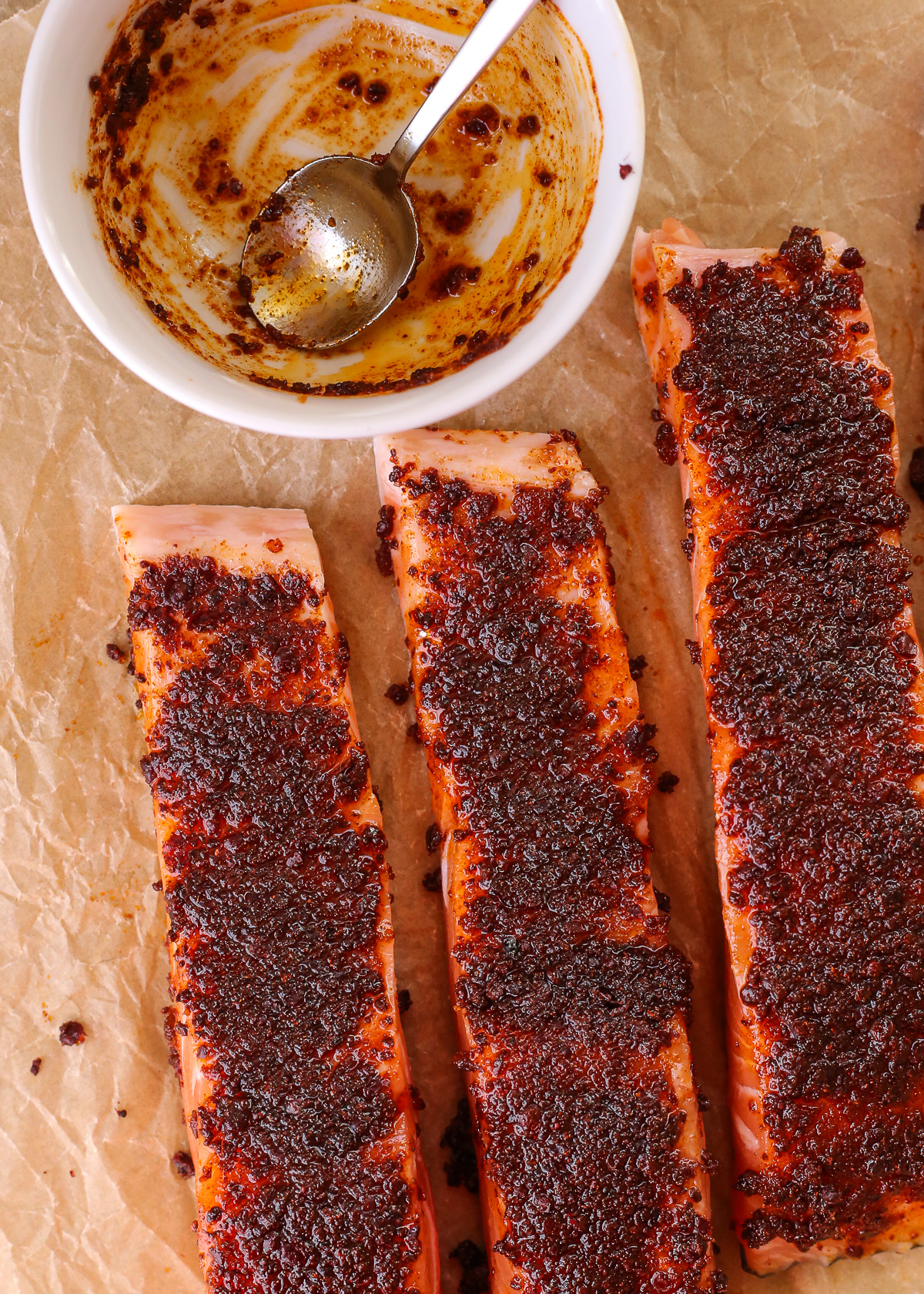 Uncooked salmon fillets coated with a deep red sumac seasoning, arranged on a piece of brown parchment paper ready to be baked in the oven or air fryer.