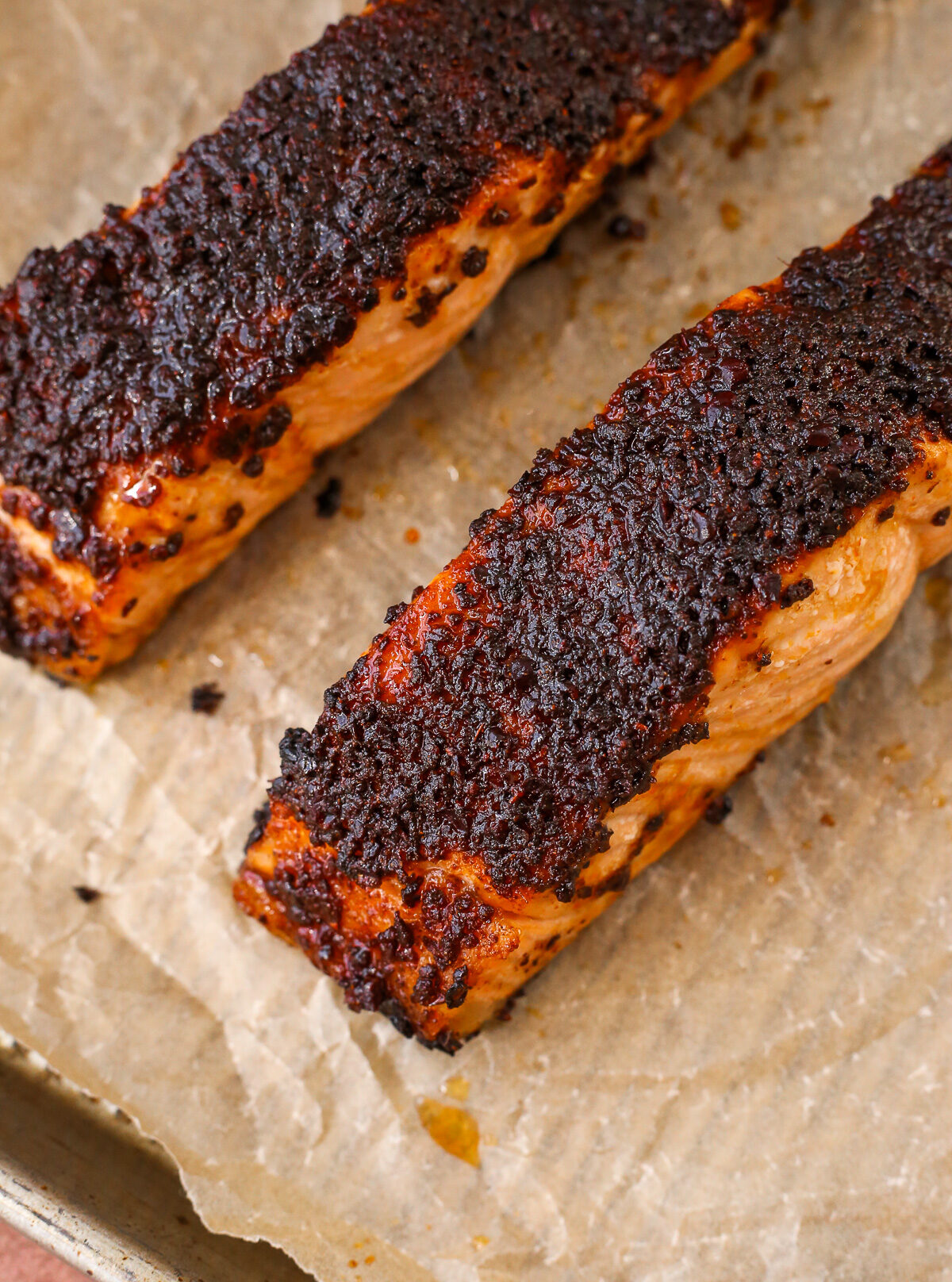 A close view of a cooked salmon fillet on a parchment paper-lined baking sheet, with a deep red sumac seasoning on top.