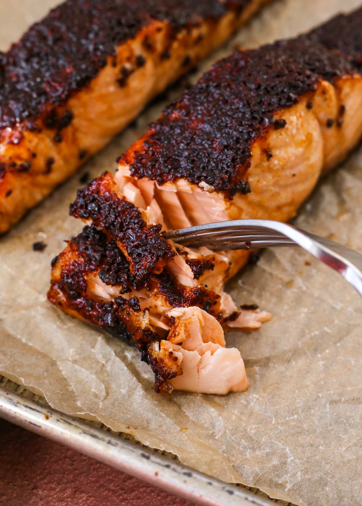 A fork pierces a cooked salmon fillet with a deep red sumac seasoning on top, showing the flaky texture.