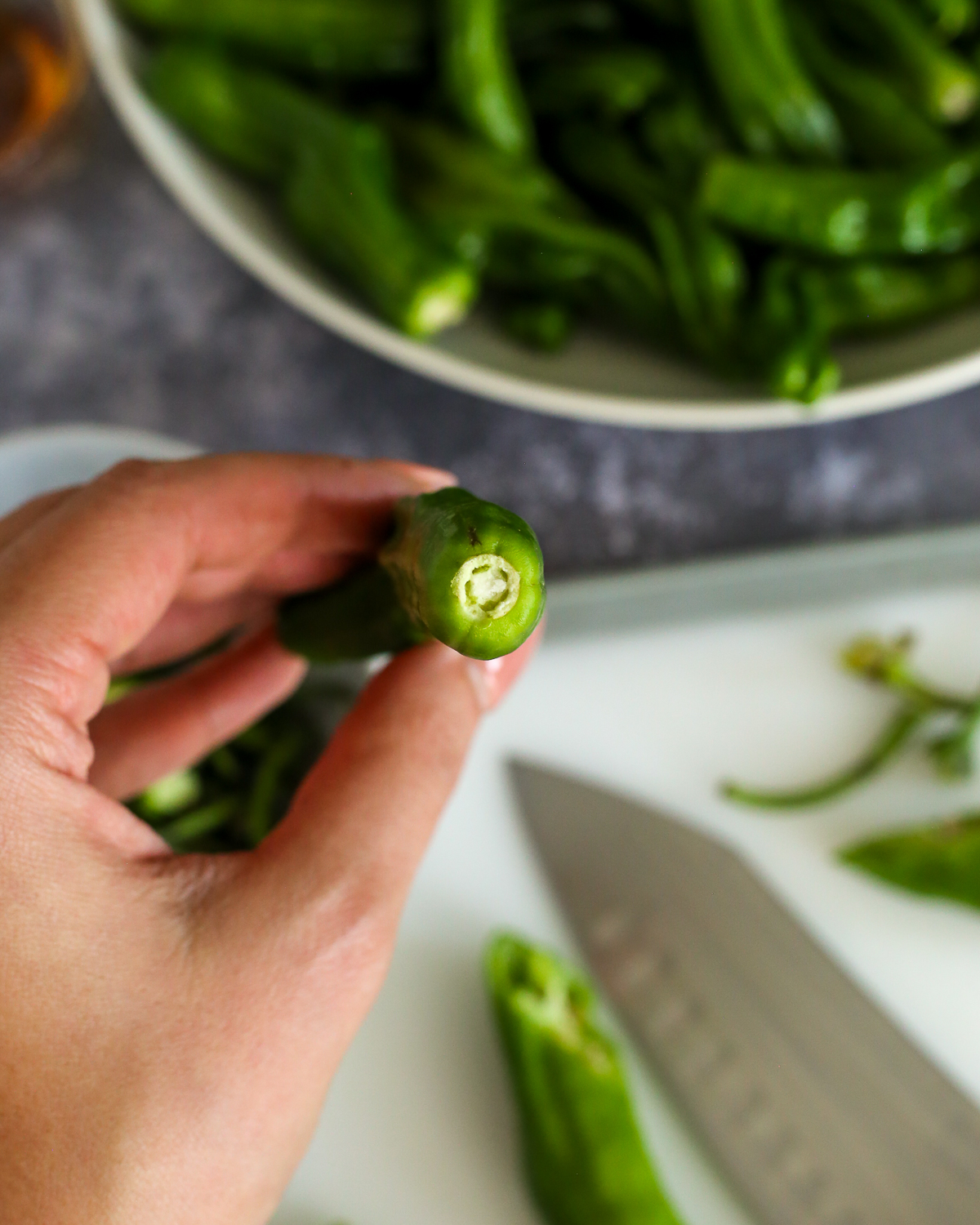 A woman's hand holding a fresh shishito pepper with the stem removed.