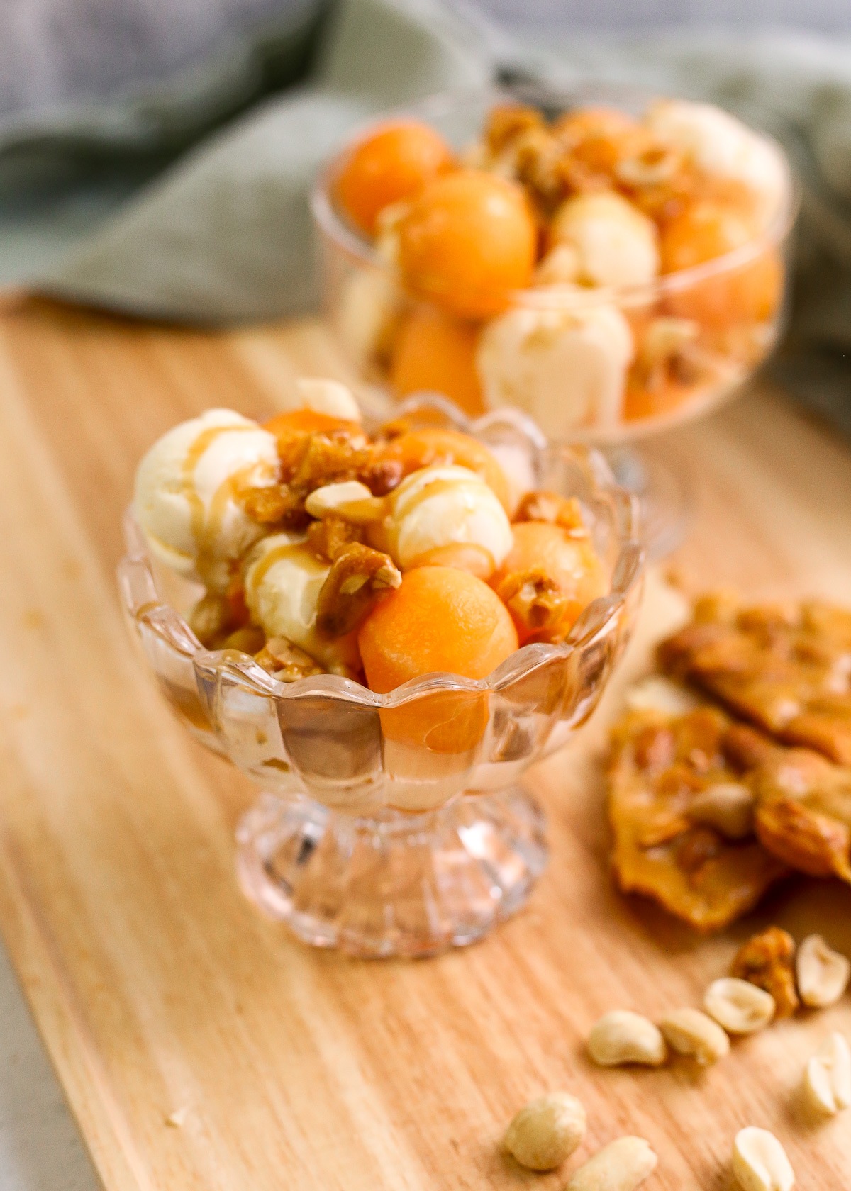 Two glass serving dishes containing cantaloupe and caramel ice cream sundaes are displayed on a wooden serving tray.