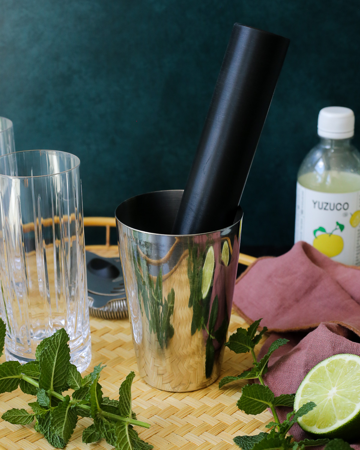 A muddle rests in the bottom of a cocktail shaker, with fresh mint sprigs scattered nearby. 