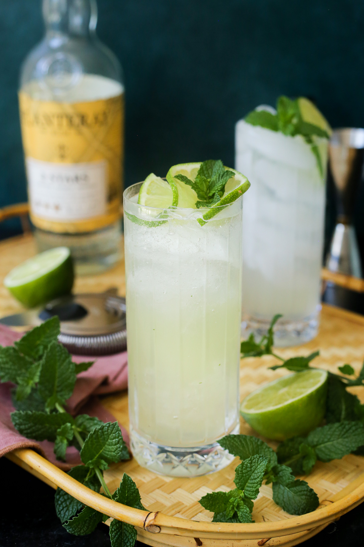 A freshly shaken yuzu mojito served in a highball glass, garnished with lime and fresh mint, served on a tray with fresh mint and extra lime. 