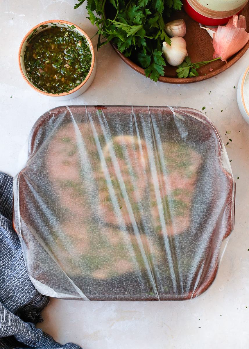 Marinating chimichurri pork chops in a shallow dish sealed tightly with plastic wrap. 