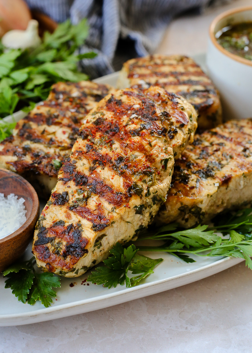 Grilled chimichurri pork chops on a serving platter, with prominent grill marks. 