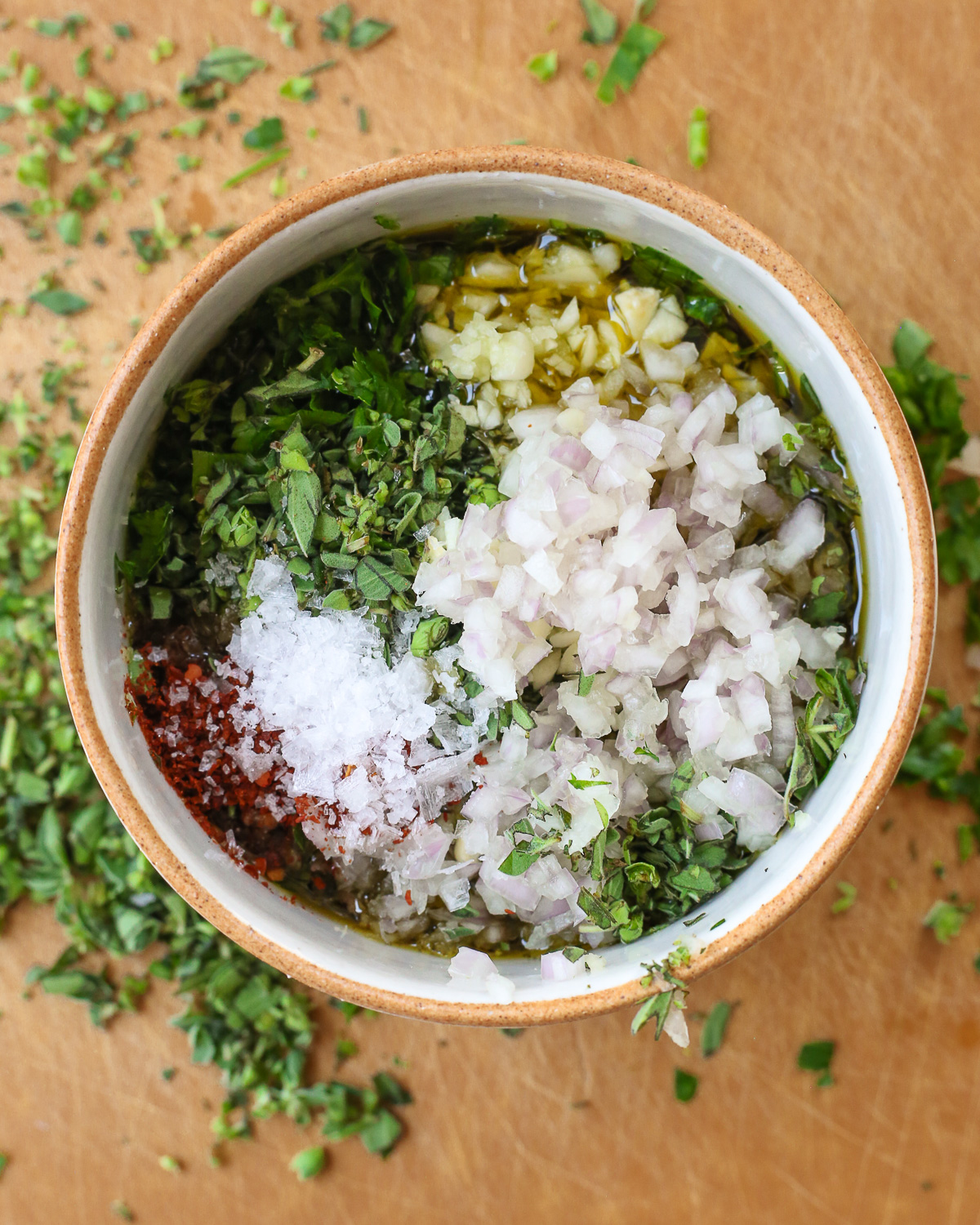 A small bowl filled with olive oil, chopped herbs, minced garlic and shallots, and a pinch of salt and red pepper flakes. 