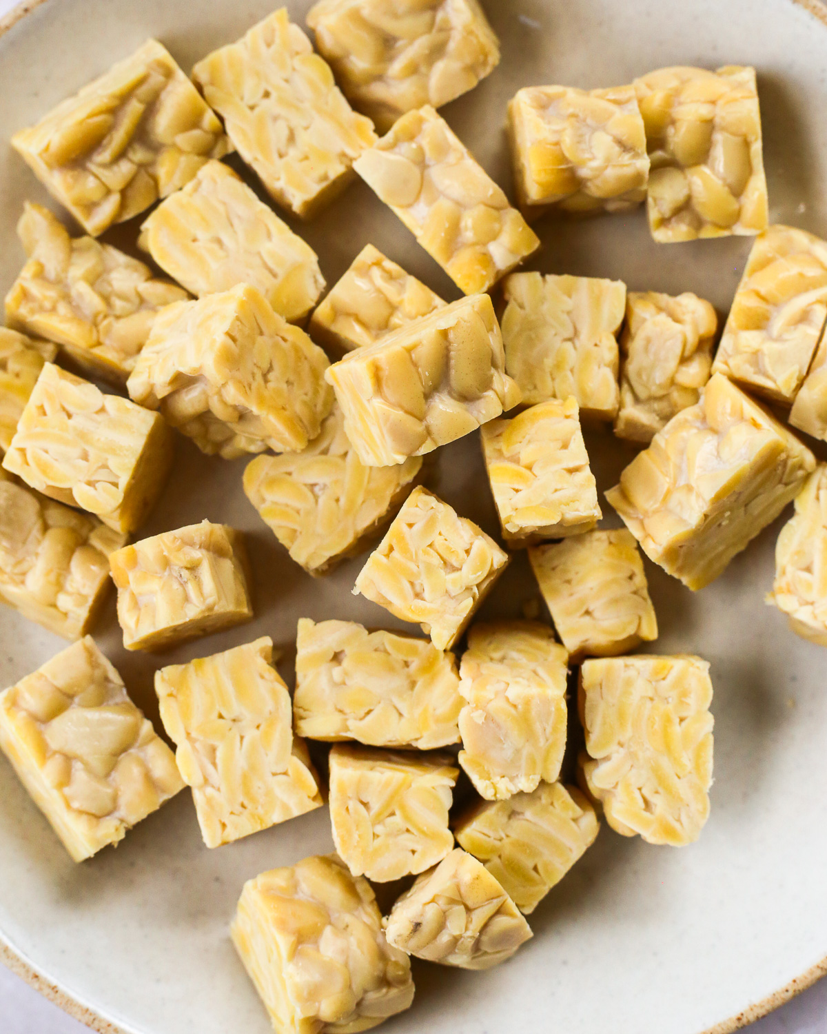 Uncooked tempeh, cut into bite sized cubes, in a single layer on a plate.