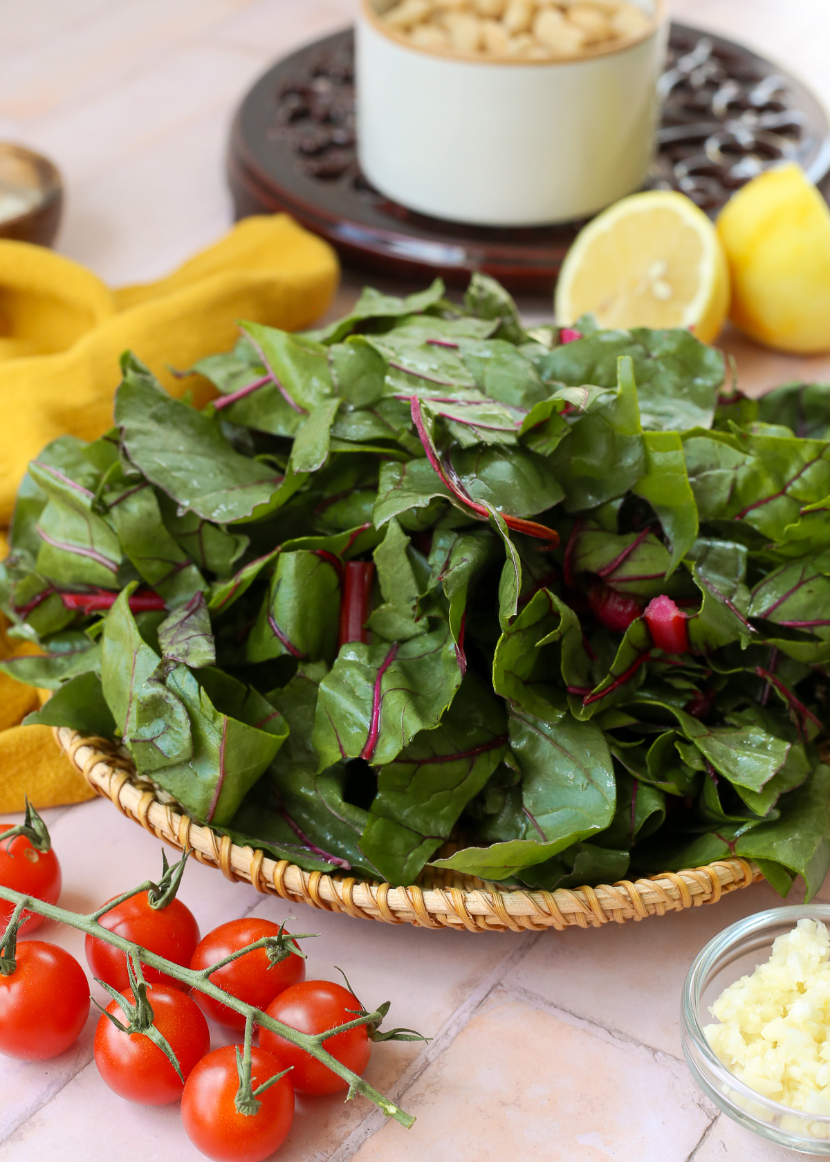 Fresh chard chopped and prepped on a dish, surrounded by cherry tomatoes and a sliced lemon. 