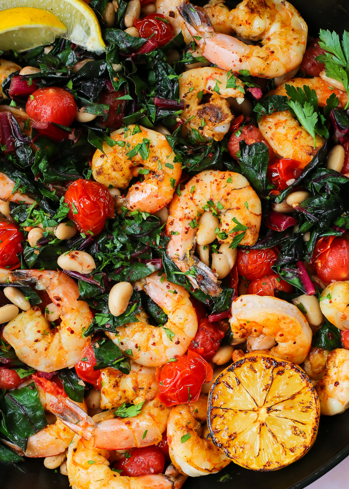 Seared shrimp, seasoned with red pepper flakes and lemon zest, in a bed of cooked greens with blistered tomatoes and white beans. 