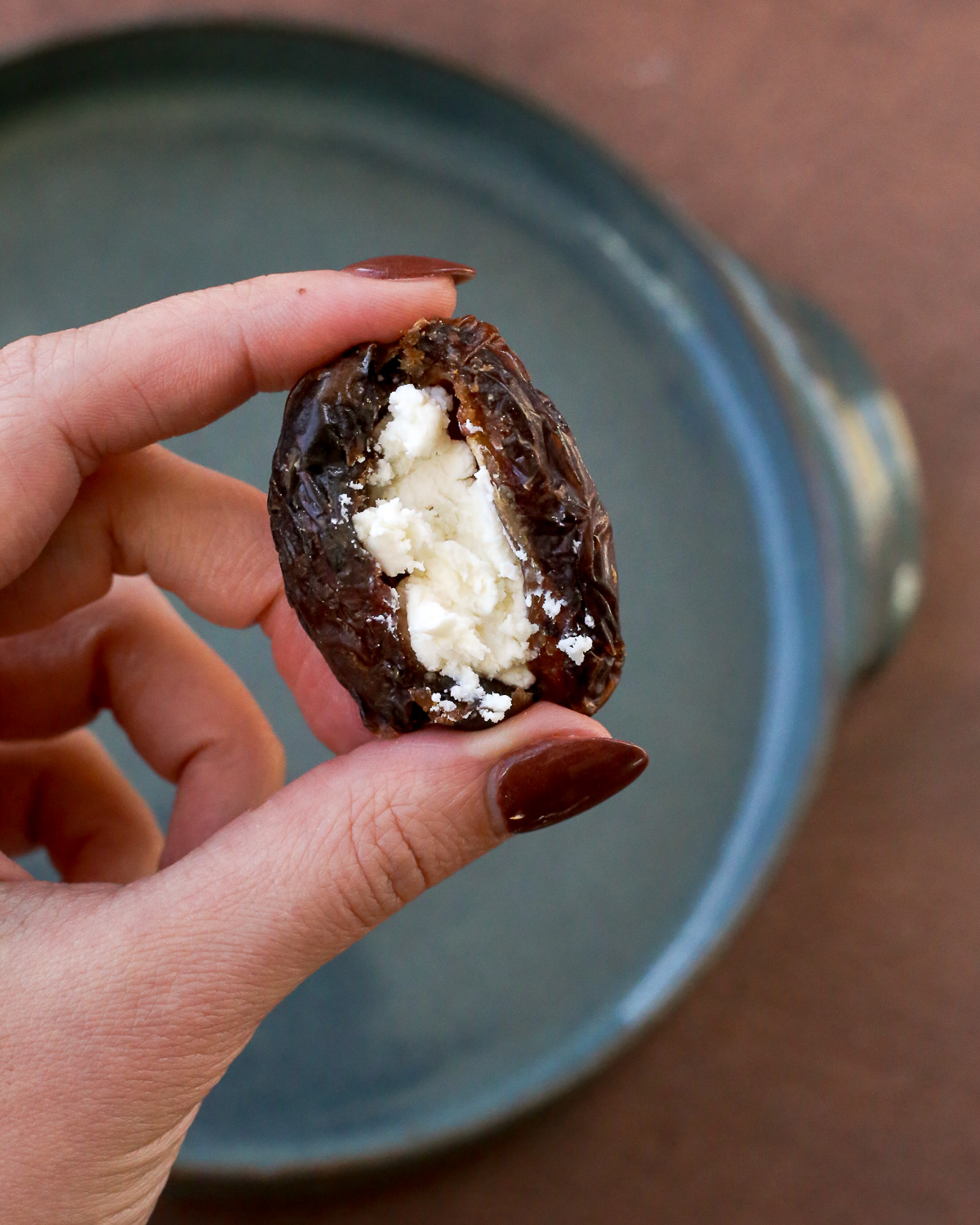 A woman's hand holds a pitted Medjool date, stuffed with a small amount of creamy goat cheese. 