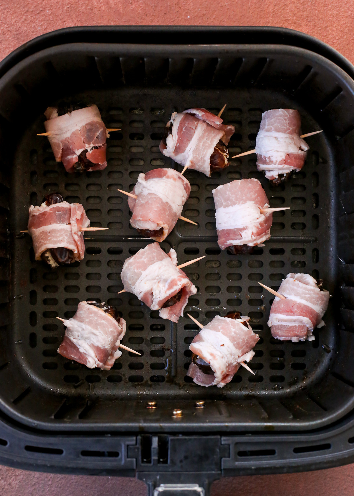 The basket of an air fryer filled with uncooked bacon wrapped dates.