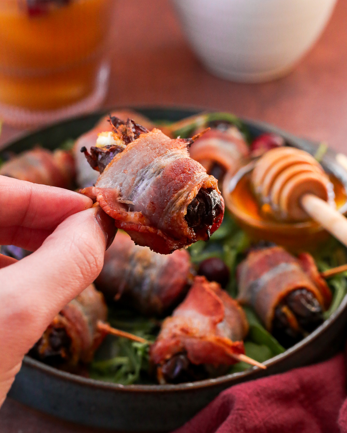 A woman's hand holds a bacon wrapped dated stuffed with cheese.