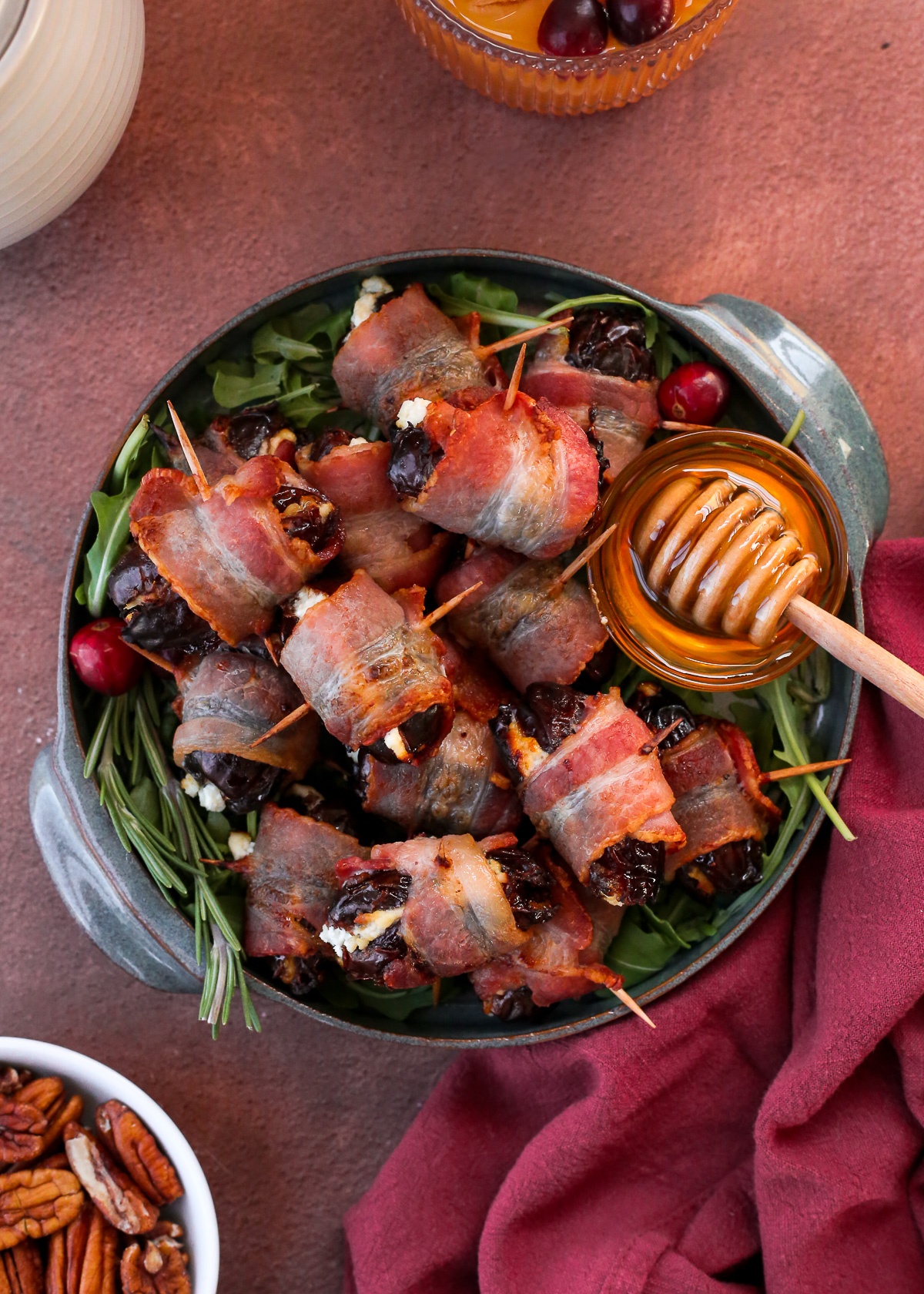 A pile of bacon wrapped dates stuffed with goat cheese, served on a small ceramic platter.