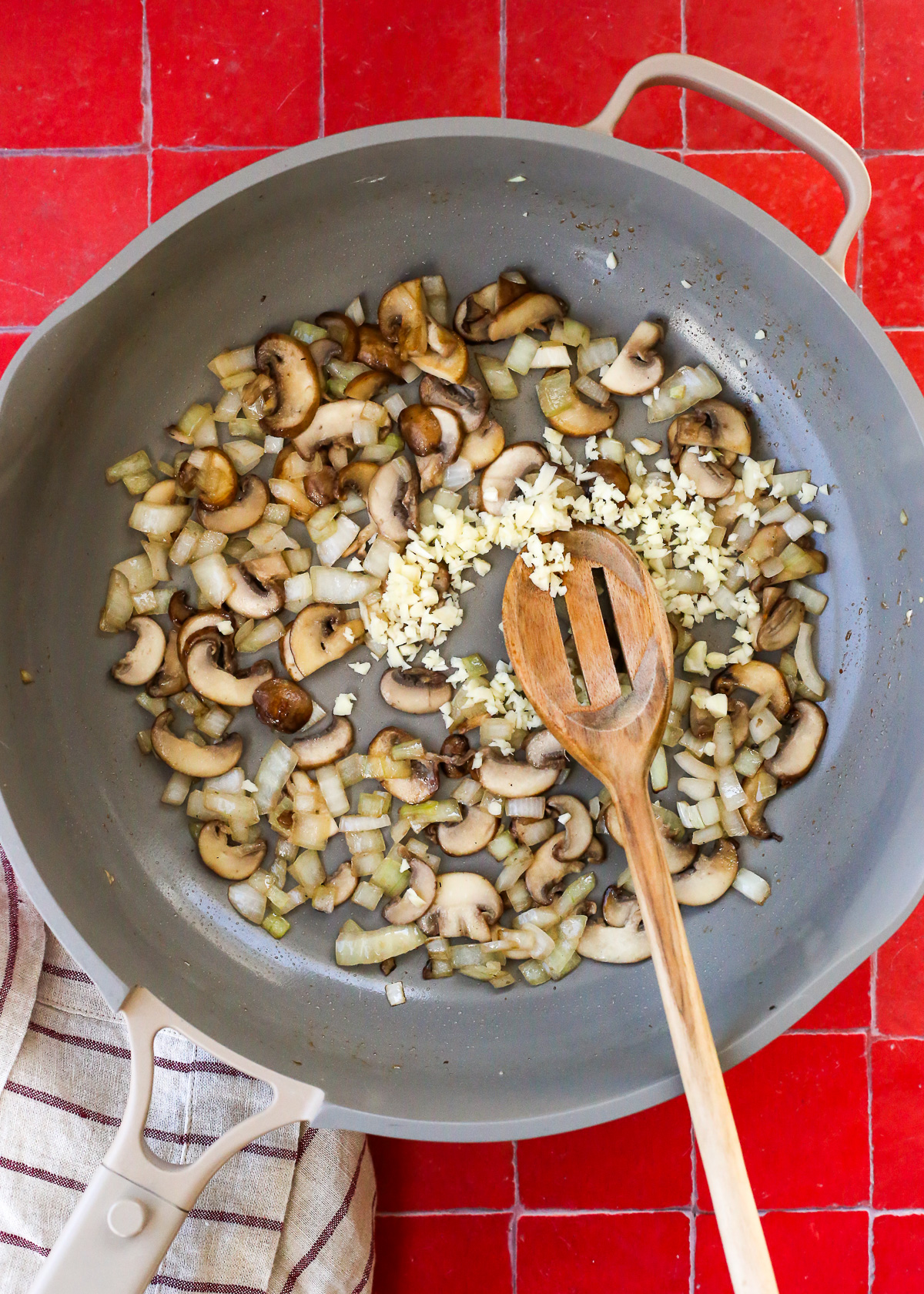 Diced onions and sliced mushrooms cooking in a saute pan, with minced garlic added. 