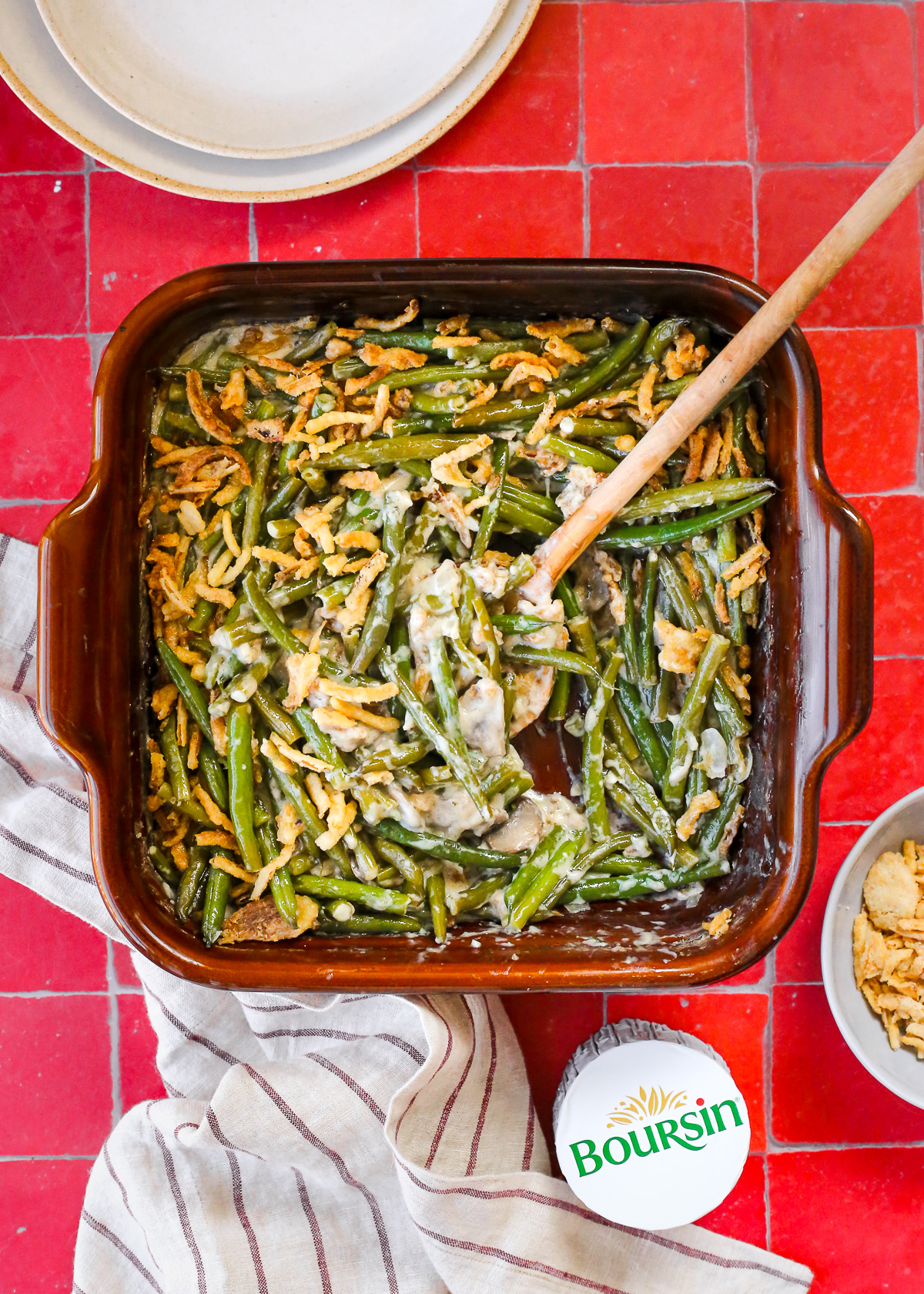 A square casserole dish filled with a homemade green bean casserole made with Boursin cheese, topped with fried onions.