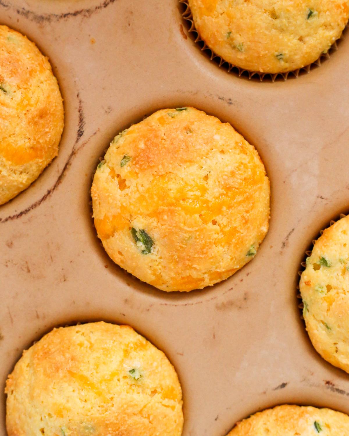 A freshly baked cheesy jalapeno cornbread muffin with a golden brown top and visible flecks of green  jalapenos. 
