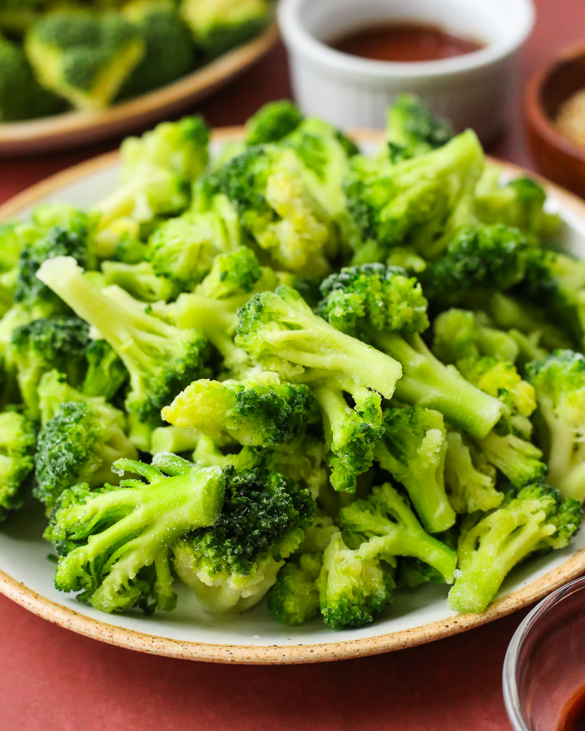 A large pile of frozen broccoli florets displayed on a kitchen countertop with small prep bowls in the background.