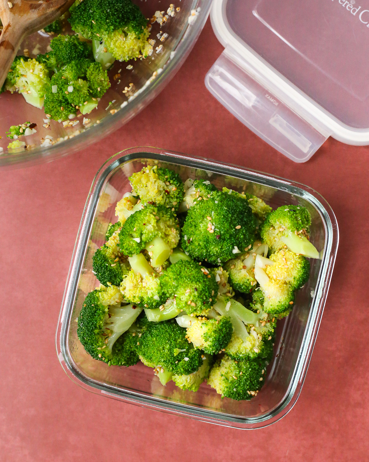 A Korean broccoli side dish in a glass storage container with the lid resting on the countertop nearby. 